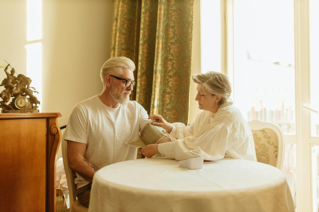 pexels-photo-8088854-8088854 An elderly couple checks blood pressure using a digital monitor at their home table.
